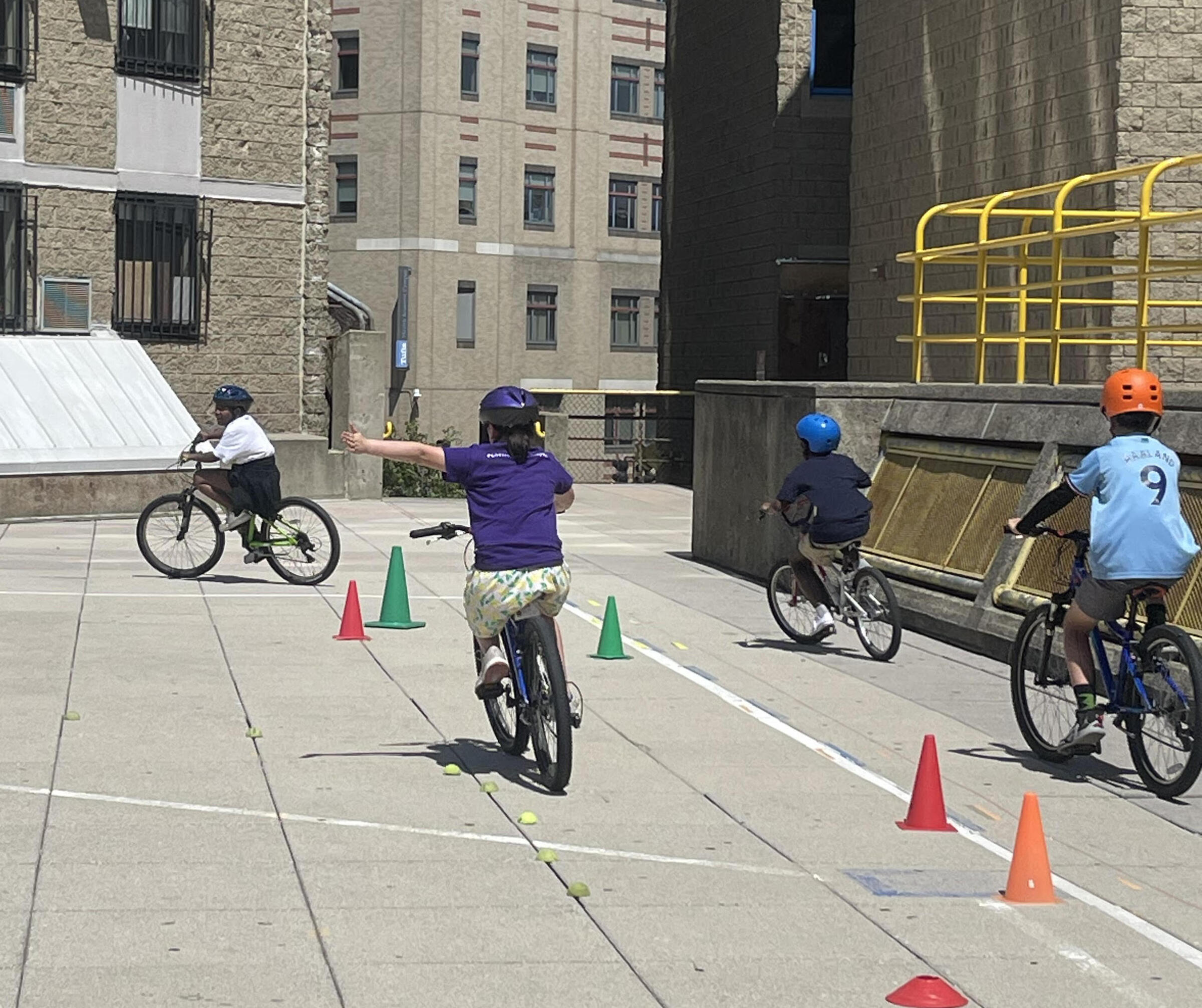 Children riding bikes and practicing hand turn signals in schoolyard. 