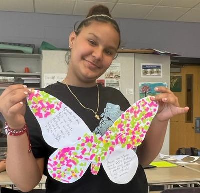 Student smiling and holding up a decorated butterfly for Immigrant Heritage Month