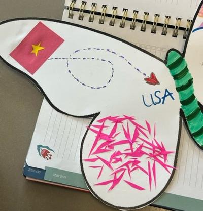 Butterfly decorated with the Vietnam flag and an arrow to the USA. The butterfly also has pink shavings on a wing and a green and black body.