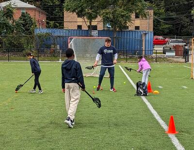 A photo of one adult and three youth playing lacrosse on a turf field 