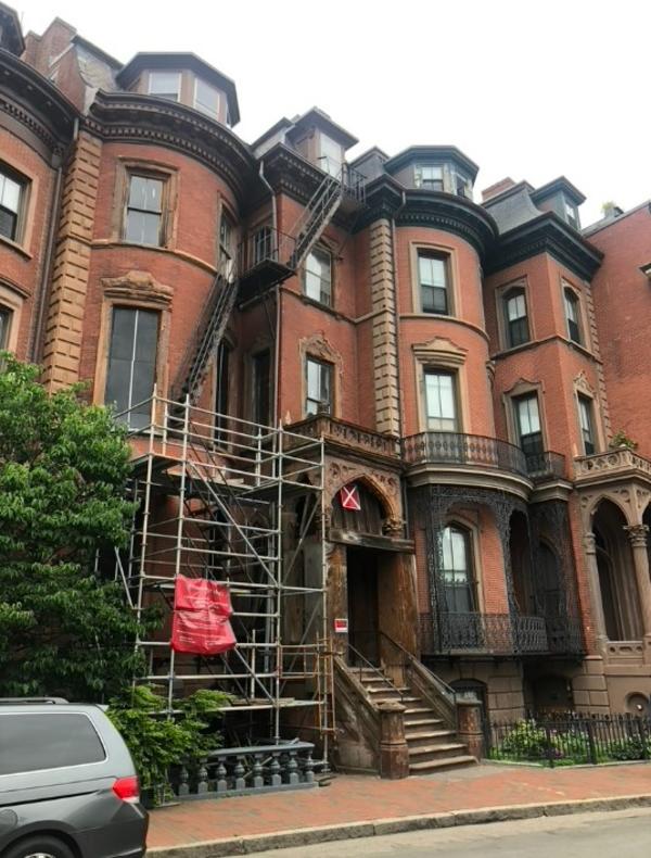 View of the front façade of an ornate 1850s South End brownstone building with scaffolding on the outside