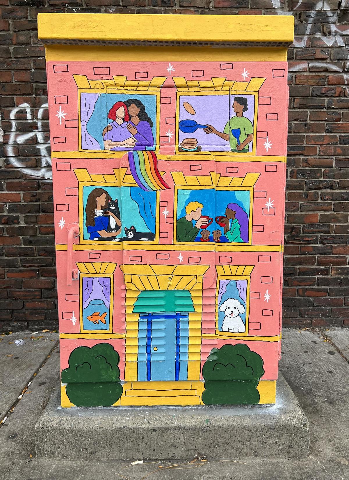 Utility box painted to look like a brightly colored building with happy people together in the windows