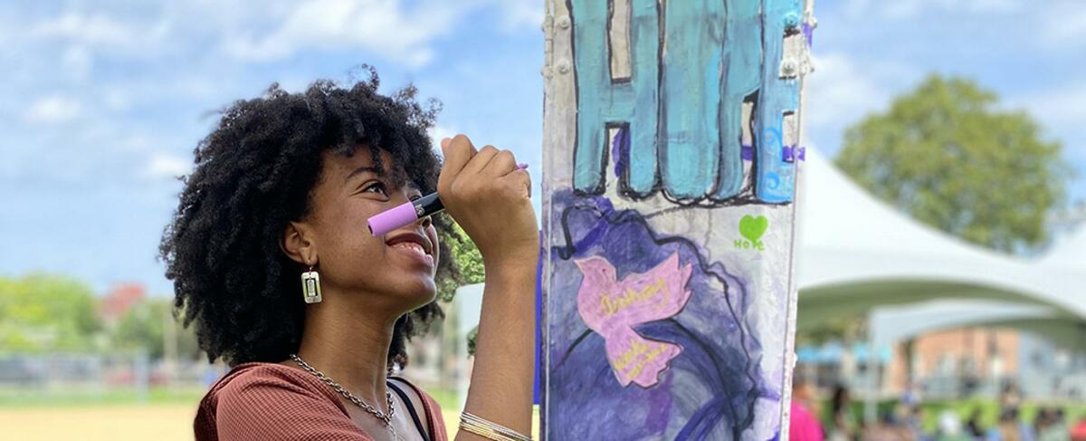 A woman draws on a pole with artwork covering it, the word "Hope" written on the pole in the foreground