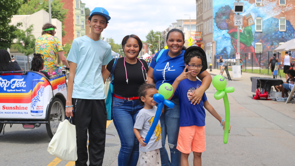 a photo showing a two adults and three children smiling and hugging on a car-free street 