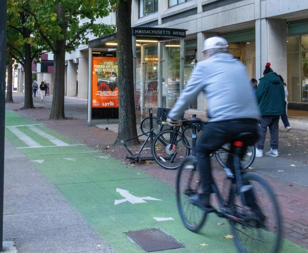 Biker on a bike path traveling in front of a bus stop with a bike rack 