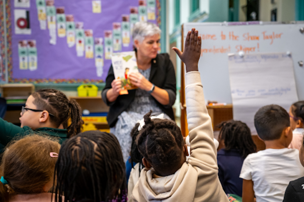 Kristin McSwain pointing to a book as children raise their hands