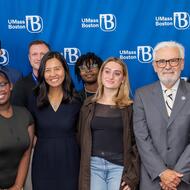 Boston Public Health Commission, UMass Boston, and City leaders come together for a photo in front of a blue UMass Boston step and repeat.