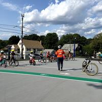 Boston Bikes staff member teaching a group of young children safe biking skills at Ross Playground