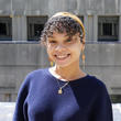 Headshot of Amber Torres, a woman with dark skin and curly hair, wearing a headband and blue sweater.