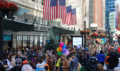 A large crowd of people on Summer Street under American flags. A woman holds balloons at the center.