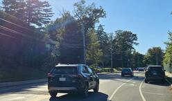 Two people walking and laughing on a sidewalk towards the camera along Beacon Street as a car passes by them.